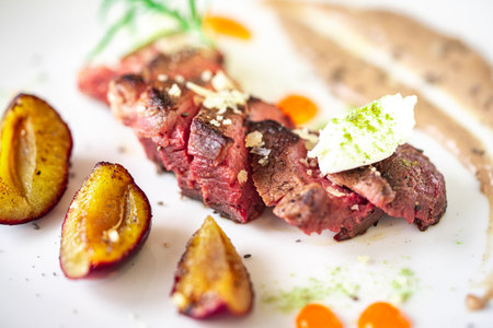 Medium-rare steak, sliced, with dogwood sauce on a white plate with roasted plums and rosemary cream cheese dumplings. Top view. High quality photoの写真素材
