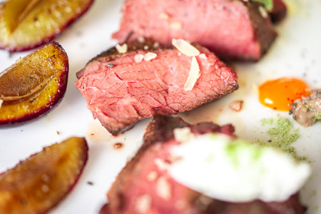 Medium-rare steak, sliced, with dogwood sauce on a white plate with roasted plums and rosemary cream cheese dumplings. Top view. High quality photoの写真素材