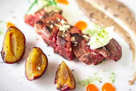 Medium-rare steak, sliced, with sauce on a white plate with roasted plums and rosemary cream cheese dumplings. Top view. High quality photoの写真素材