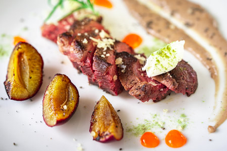 Medium-rare steak, sliced, with sauce on a white plate with roasted plums and dumplings. Top view. High quality photoの写真素材