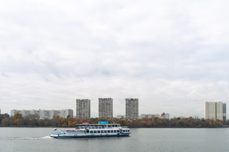 Moscow, Russia - October 17, 2025: A river cruise ship or river boat sails along the river against the backdrop of an autumn cityscape. High quality photoのeditorial素材