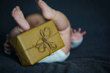 Newborn baby with a gift wrapped in brown paper on a dark backgroundの写真素材