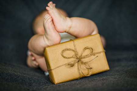 Newborn baby holding a gift wrapped in brown paper with a bow