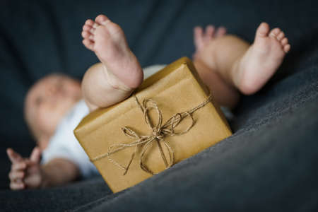 Newborn baby with a gift wrapped in brown paper and tied with twineの写真素材