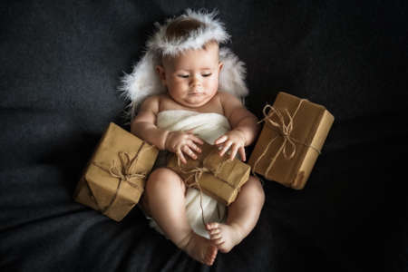 Cute newborn baby in angel costume with gift boxes on black backgroundの写真素材