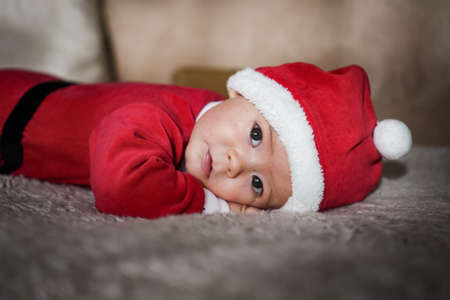 Portrait of cute little baby in red Santa Claus costume lying on the floorの写真素材