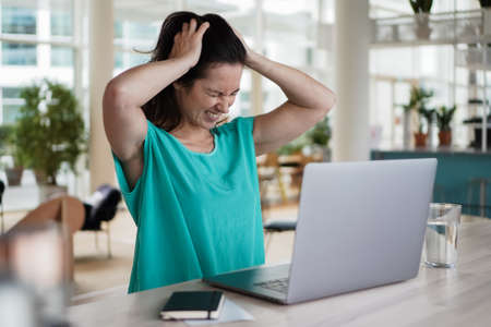 sad depressed remote working woman sitting disappointed with headache infront of a laptop or...