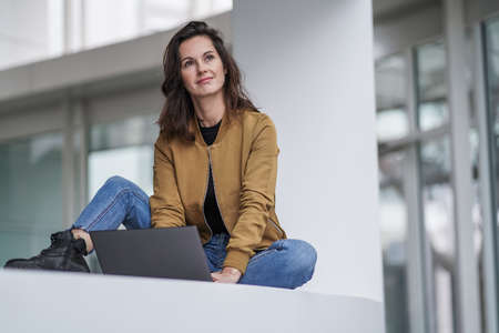 happy beautiful student woman working remotely in front of a notebook in casual jeans outfit in a...