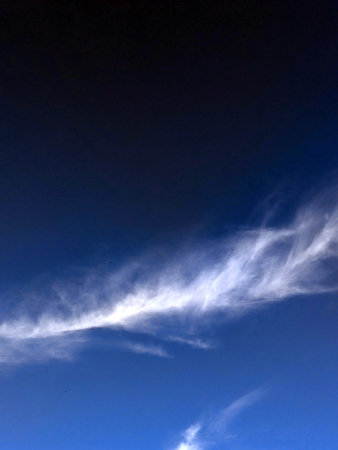 Close up of atmospheric blue black sky with whispy white clouds
