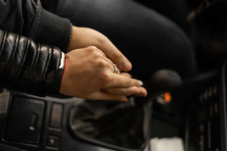 hands of a guy and a girl in a car, a guy with a girl in a car hold hands while driving on the road, an unrecognizable girl touches a guy's hand while he is driving a car, framing, selective focus, romance conceptの写真素材