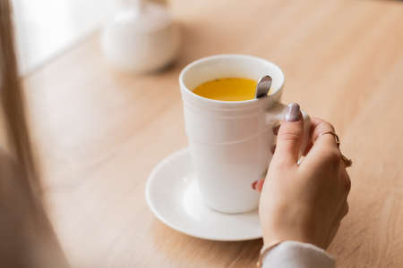 hand with a white cup, close-up white cup on a saucer holds the girl in her arms in the office during a break. Image with selective focus, female hands holding a cupの写真素材