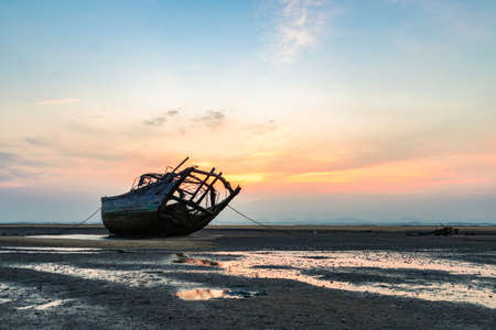 Sprinkled on the beach in the setting sun, a ship that has experienced strong winds and waves is shelved by the seaの写真素材
