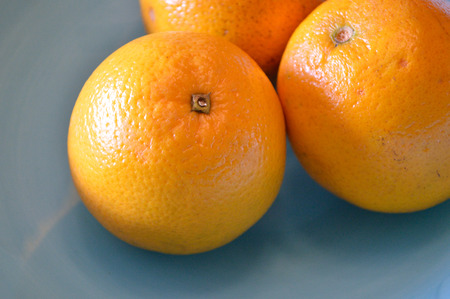 Closeup of 3 valencia oranges in a sky blue bowlの写真素材