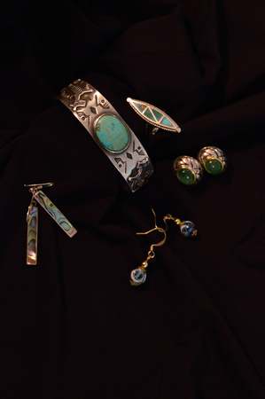 Silver and turquoise cuff bracelet, silver and turquoise ring, glass earrings, and other unknown stones. Jewelry against black fabric backgroundの写真素材