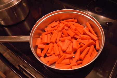 Chopped fresh carrots in stainless steel pan on black stovetopの写真素材