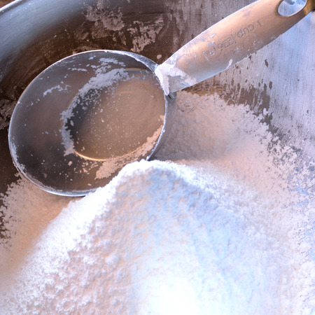 Square photo of a stainless steel measuring cup in a bowl of confectioner's sugar, freshly sifted.の写真素材