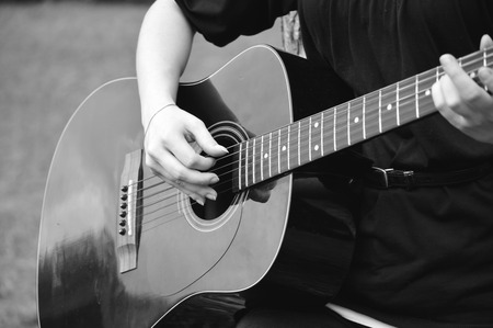 Young woman playing a black acoustical guitar in outside setting.の写真素材