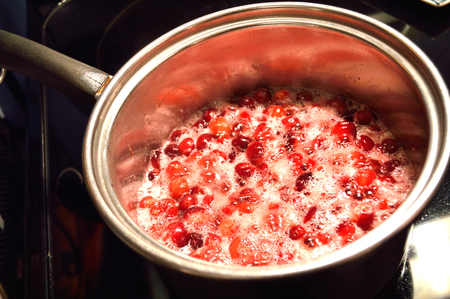 Bright red cranberries cooking in a stainless steel pot on stovetop, to make whole-berry cranberry sauce.の写真素材