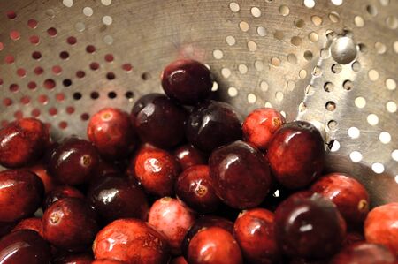 Bright red cranberries in a metal colander being washed and prepared to cook with.