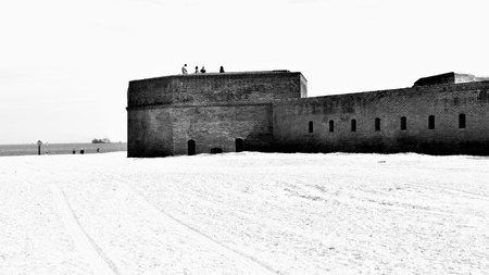 Black and white image of a historical military brick fort in America, on a sandy beach