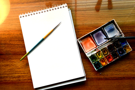 Art supplies: pad of watercolor paper, watercolor pallate with cakes of watercolor paint and two paintbrushes, ready to begin painting with. Real art supplies in a real artist's studioの写真素材