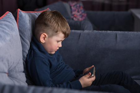Little boy with smartphone sitting on sofaの写真素材
