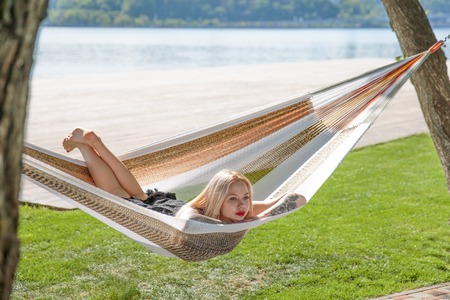 Young blonde woman resting on hammock On a background of green grass and blue skyの写真素材