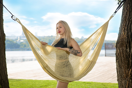 Young blonde woman resting on hammock On a background of green grass and blue skyの写真素材