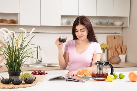 Woman Reading Magazine and drinking tea In Kitchen At Homeの写真素材