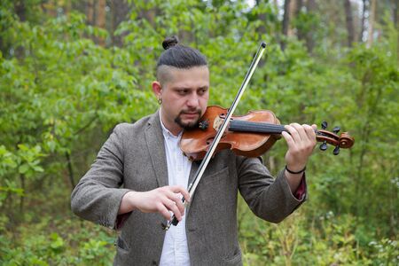 Handsome man playing the violin on nature backgroundの写真素材