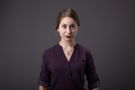 Stylish young businesswoman with a friendly expression looking directly at the camera, closeup of her face on a grey background with copy spaceの写真素材