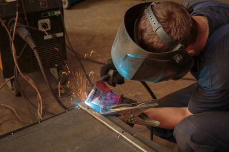 Male in face mask welds with argon-arc welding in body shopの写真素材