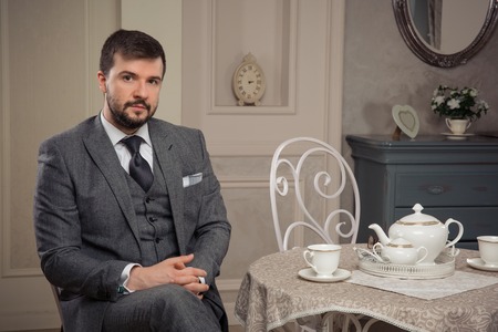 handsome old-fashioned bearded man sitting at the table in vintage furnishings in studioの写真素材