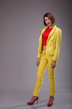 Glamour fashion style catalog casual clothes for business woman meeting date walk party sexy beautiful woman brunette shot hair wear yellow costume perfect body shape model suit. Studio shoot over gray backgroundの写真素材