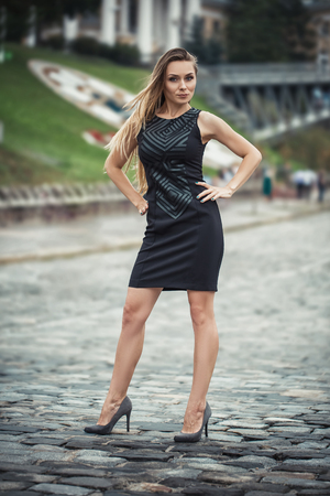 Fashionable city girl concept. Gorgeous young woman walking in city wearing summer black clothes. Autumn. Rainy dayの写真素材