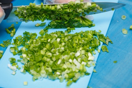 Hands of cheaf cutting a green onion. A chopped green onions on a wooden board with a knife.の写真素材