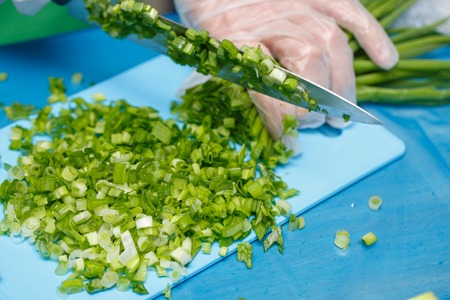 Hands of cheaf cutting a green onion. A chopped green onions on a wooden board with a knife.の写真素材