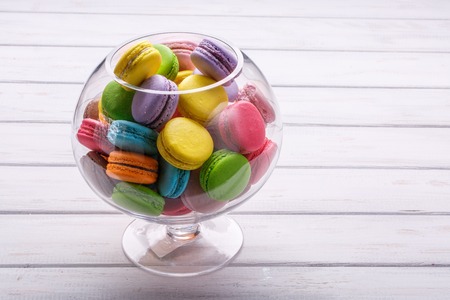 large glass vase full colorful macaroons over white wooden bsckground. Place for the textの写真素材