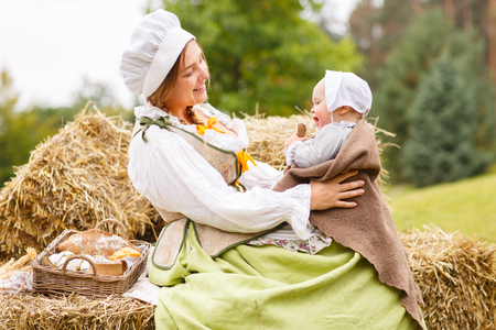 Happy peasant mother with little baby in summer playing on haystack in the fieldの写真素材