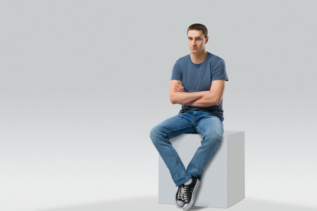 young man sitting on white cube. isolated. Space for text