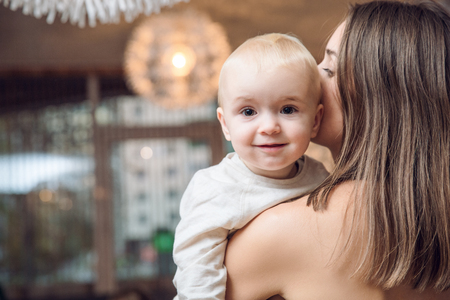 curious smyling baby looking from behind mother's shoulderの写真素材