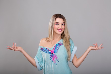Portrait of a pretty woman in blue dress with a parrot, white shirt smiles and spreads his arms to the sides standing over gray background and looking at cameraの写真素材