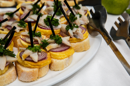 One plate with snacks on a buffet table. Selection of tasty bruschetta or canapes on toasted baguette with potatoes herring fish, red onions. restaurant feed, buffet table. New Year, Christmasの写真素材
