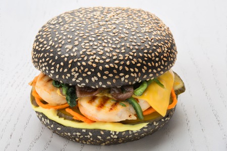 Black burger with chicken grill, pickle, spinach cheese. bun is strewed with sesame seeds over white wooden backgroundの写真素材