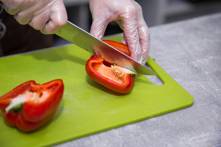 Salad preparation - hands in gloves cutting red pepper into piecesの写真素材