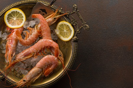 Large tiger Shrimps and slice of lemon fresh in ancient plate full of ice on dark background. Space for textの写真素材
