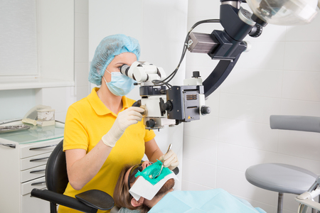 Female dentist with dental tools - microscope, mirror and probe checking up patient teeth at dental clinic office. Medicine, dentistry and health care concept. Dental equipmentの写真素材