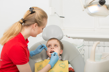 Female dentist examines the teeth of the patient child. Child mouth wide open in the dentist's chair. Close-up. Medical conceptの写真素材
