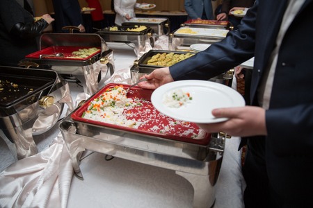 man in suits choosing food at a banquet. the man is putting rice on a buffet tableの写真素材