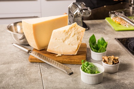 grated parmesan cheese and metal grater on wooden board with greenery in the kitchenの写真素材